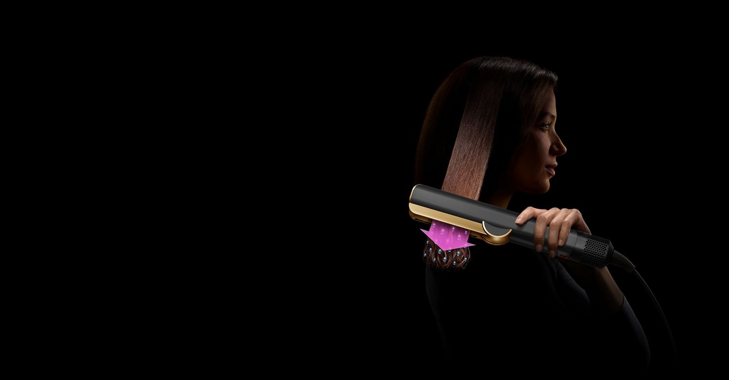 A woman uses a Dyson Airstrait straightener to dry and straighten a tress of her hair.