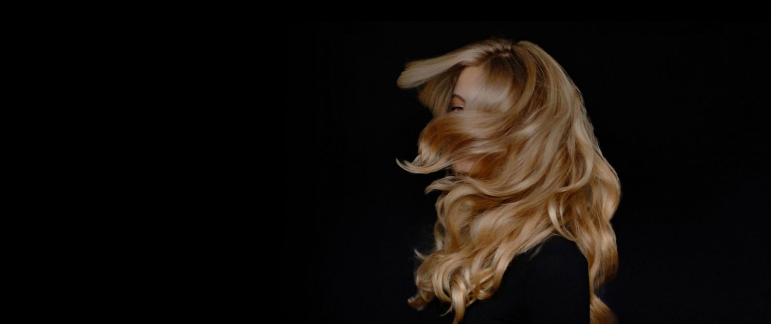 A woman uses a Dyson Airstrait straightener to dry and straighten a tress of her hair.
