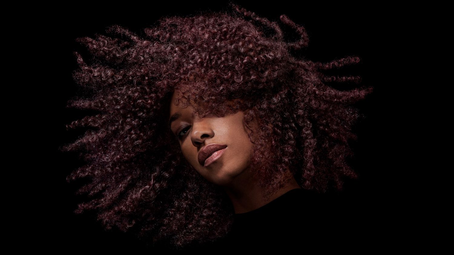 A model with dark coily hair after styling their hair with Dyson Chitosan Post-style serum.