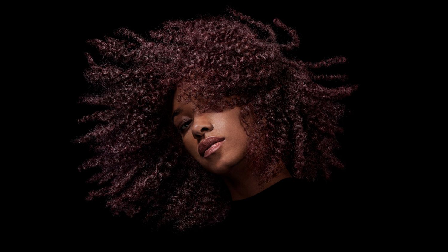 A model with dark coily hair after styling their hair with Dyson Chitosan Post-style serum.