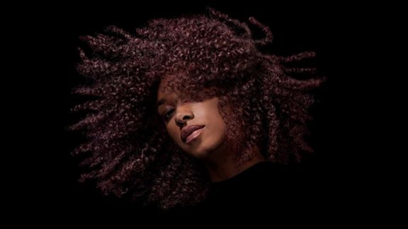 A model with dark coily hair after styling their hair with Dyson Chitosan Post-style serum.