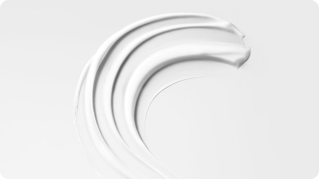 Crème de précoiffage étalée sur fond blanc, montrant la texture.