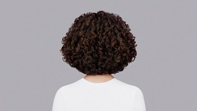 Naturlig krøllete, mørkebrunt hår stylet med Dyson Chitosan Post-style-serum og Dyson Supersonic r. Sett bakfra.