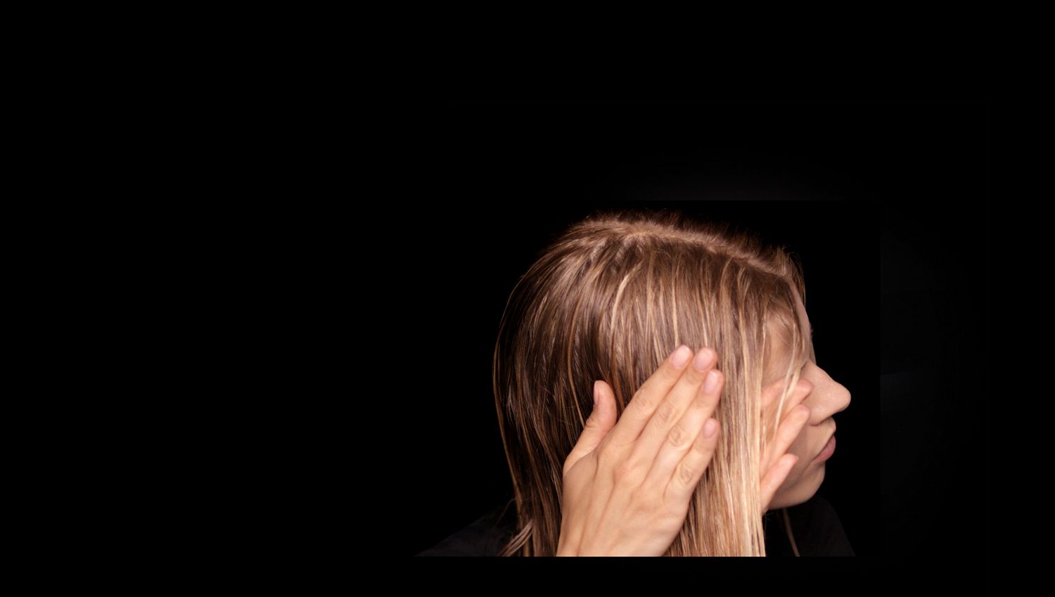 A model with long, damp hair uses her hands to smooth product through the lengths