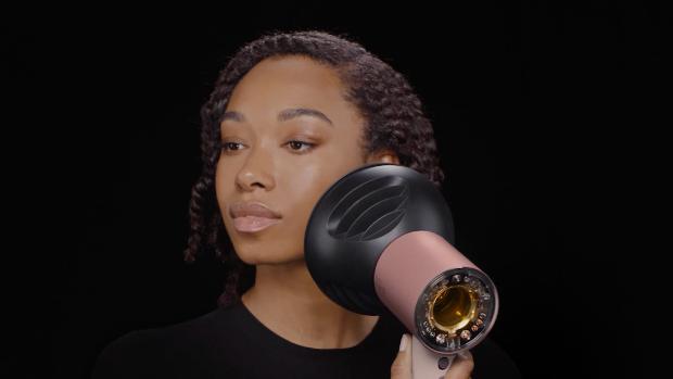 Model dries her hair with the Dyson Supersonic Nural hair dryer and diffuser.