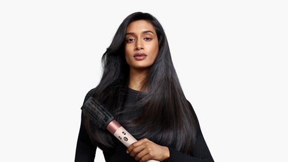 Modèle tenant le multi-styler et le sèche-linge Dyson Airwrap ID avec la brosse à boucle anti-emmêlement.