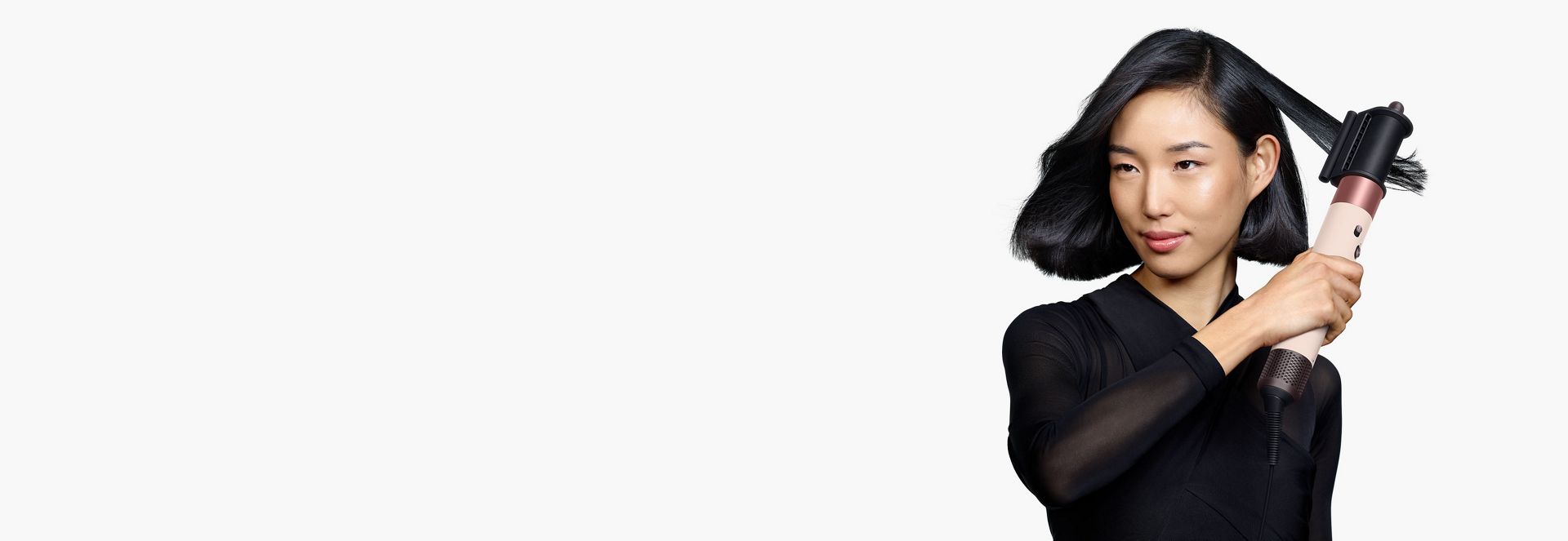 Une femme aux cheveux noirs mi-longs utilise l’embout lissant pour cheveux rebelles pour parfaire sa coiffure.