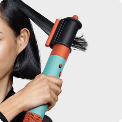 Ein rothaariges Model wird von hinten gezeigt, während sie mit dem Dyson Airwrap i.d. Locken kreiert.