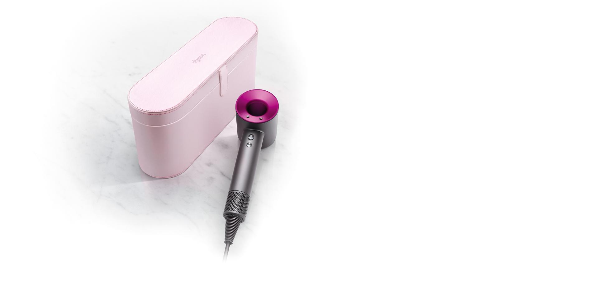 różowe etui i leżąca obok suszarka Dyson Supersonic w kolorze stal/fuksja