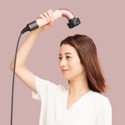 低温ツールがついたDyson supersonic rドライヤーを頭の上に持って髪を乾かす女性