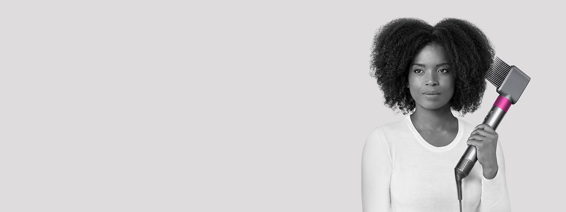 Moteris, formuojanti plaukus su „Dyson“ plačiadančių šukų priedu