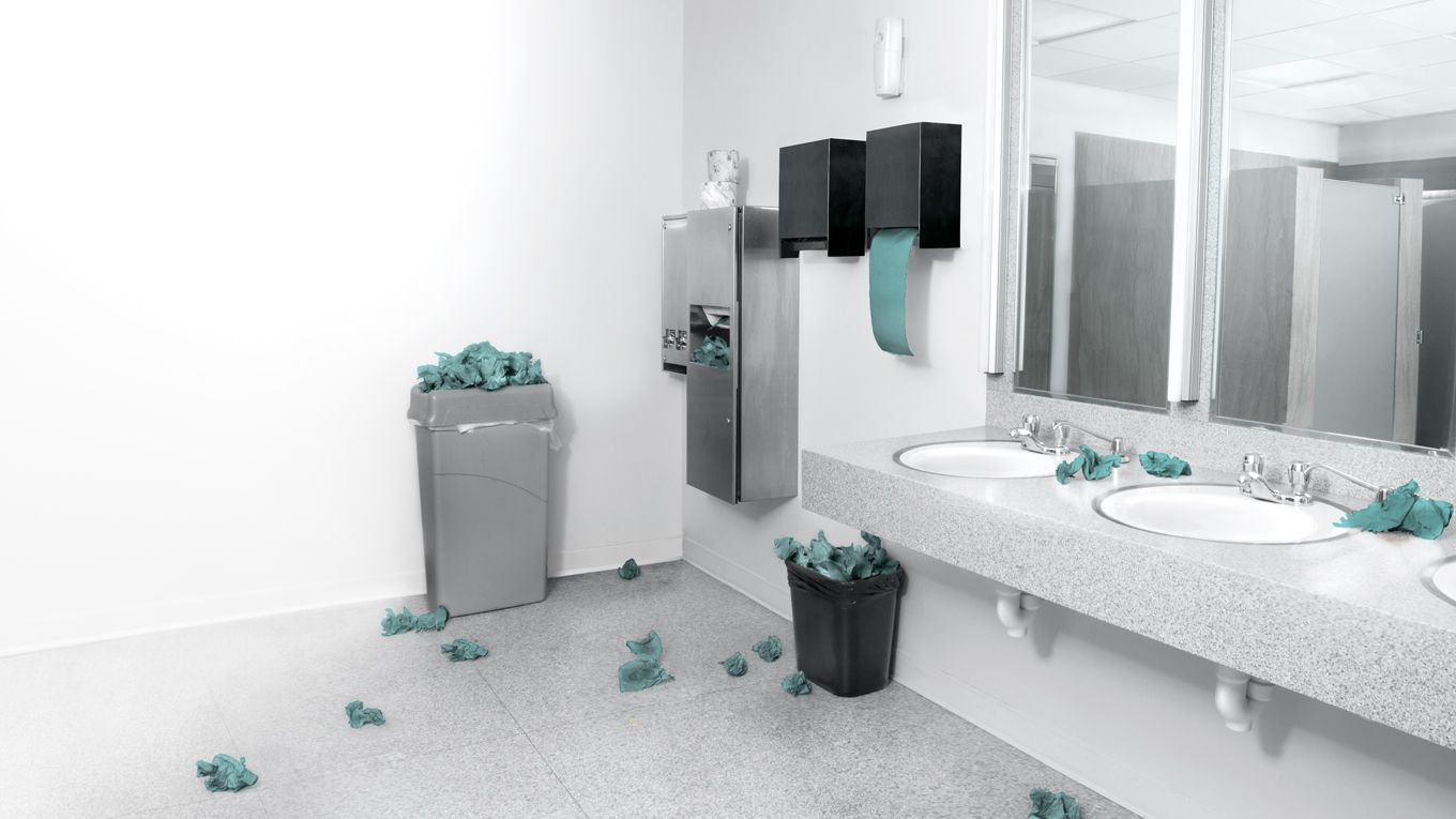 Schmutizge Papiere liegen in einem öffentlichen Waschraum auf dem Boden. 