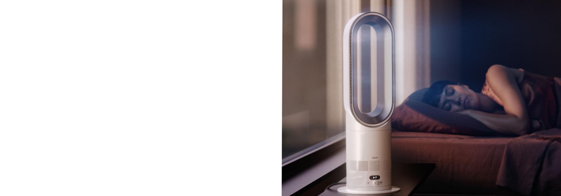 „Dyson Hot+Cool HF1“ nuotolinio valdymo šildytuvas su išankstinio šildymo funkcija ir ventiliatorius tyliai veikia miegamajame šalia miegančio žmogaus.