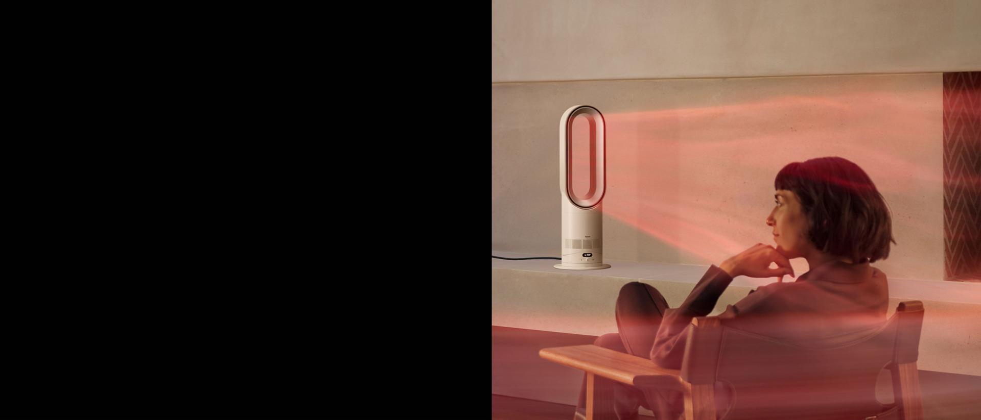 A woman sits in front of her Dyson Hot+Cool HF1 Remote Link Pre-heat heater and cooling fan as it heats the room.