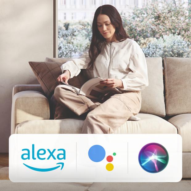 A Dyson Purifier projects air in a large living room. Logos for Amazon Alexa, Google Assistant and Siri.