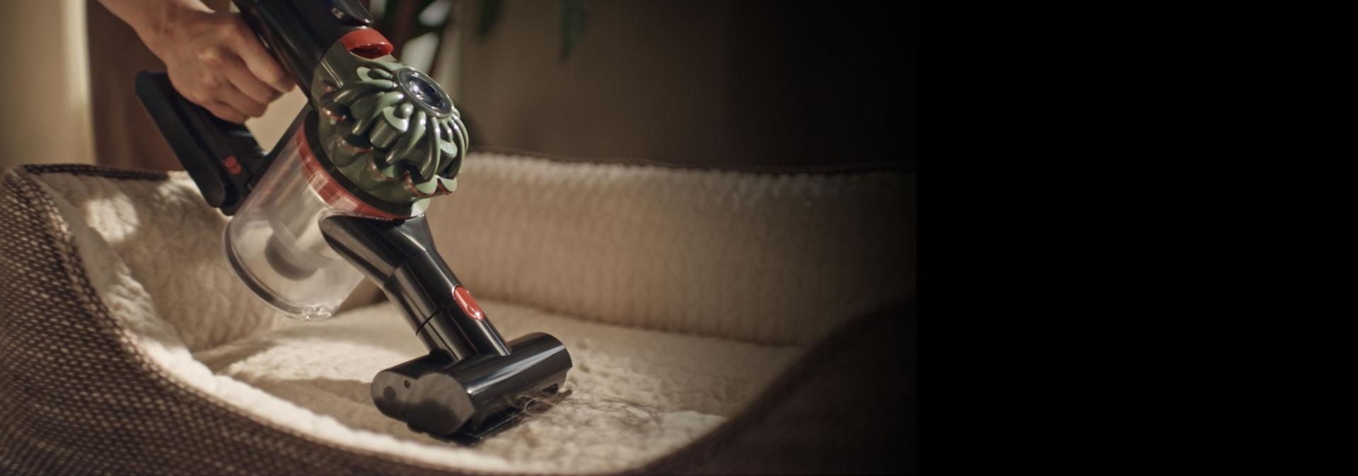 يتم استخدام مكنسة Dyson V8 Cyclone مع الأداة الصغيرة ذات المحرك لتنظيف سرير الحيوانات الأليفة.