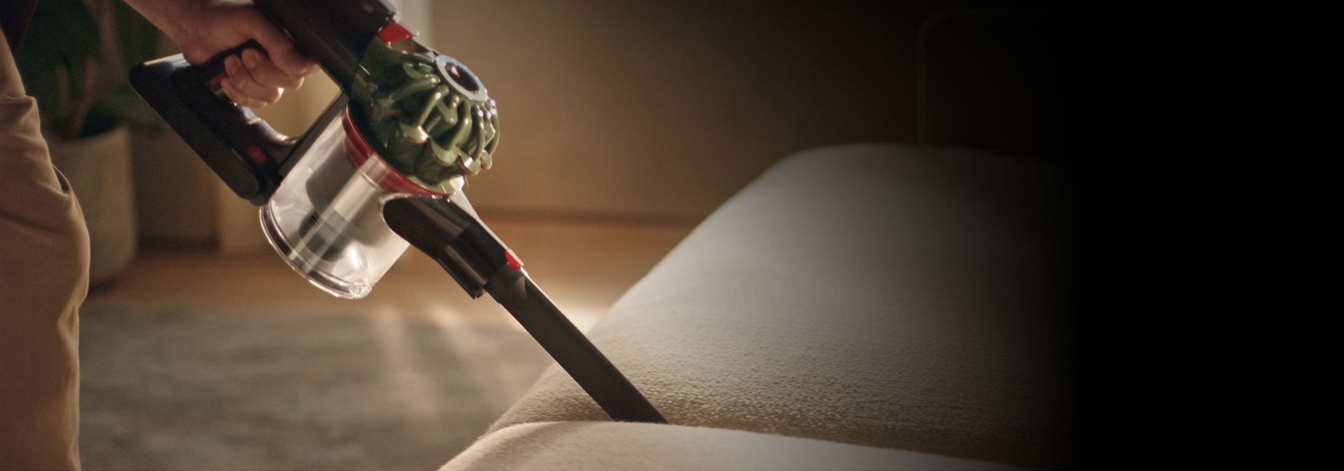 تُستخدم مكنسة دايسون V8 Cyclone مع أداة تنظيف الشقوق لتنظيف ما بين الوسائد على الأريكة.