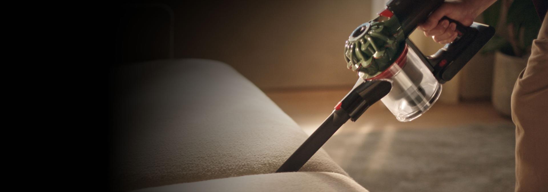 The Dyson V8 Cyclone vacuum is used with the Crevice tool to clean between cushions on a sofa.
