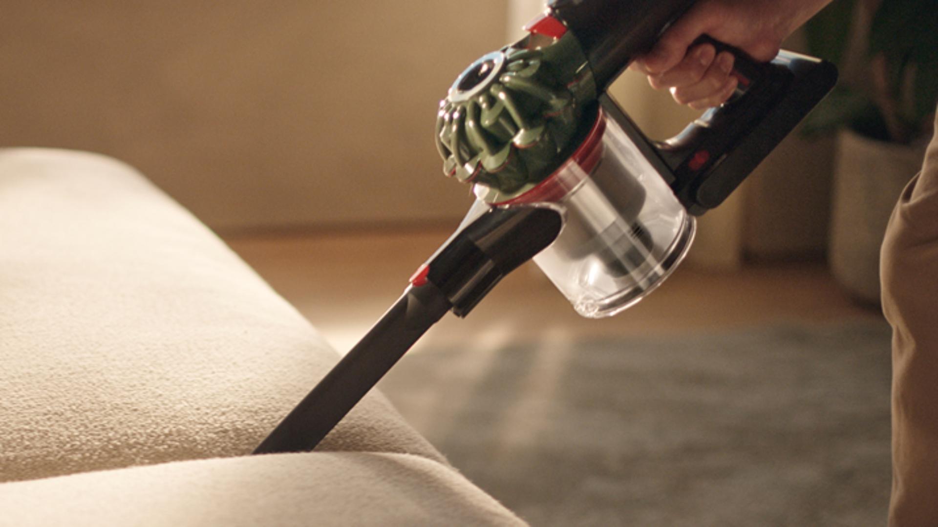The Dyson V8 Cyclone vacuum is used with the Crevice tool to clean between cushions on a sofa.