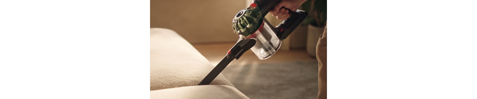 The Dyson V8 Cyclone vacuum is used with the Crevice tool to clean between cushions on a sofa.