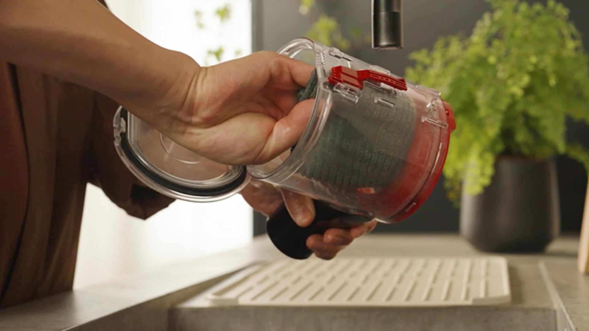 The clear bin of the Dyson V8 Cyclone vacuum is wiped clean with a damp cloth.