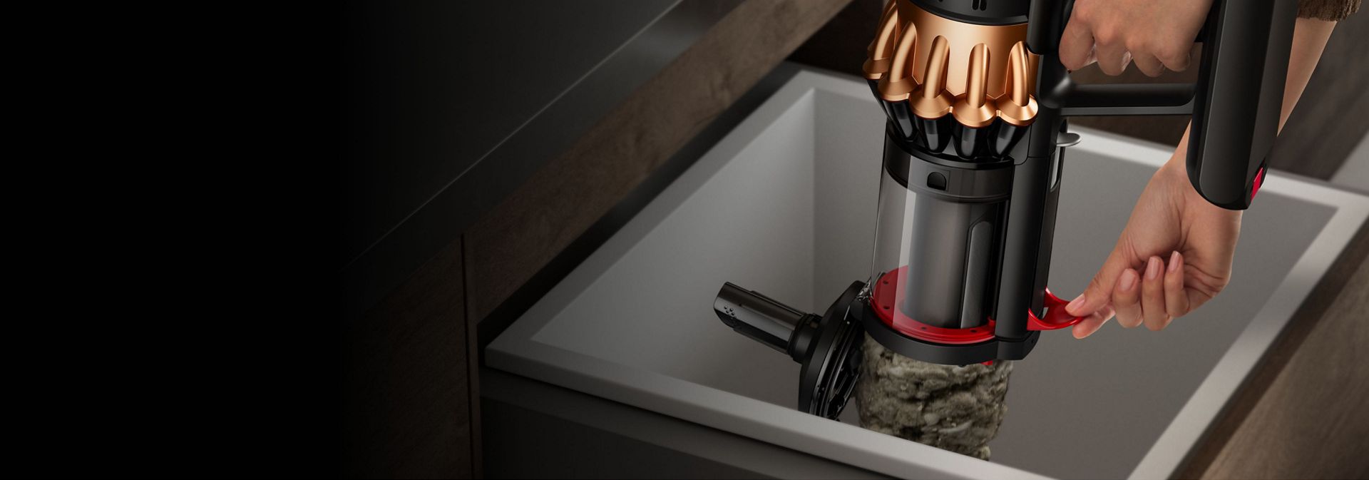 En person tørker og tømmer beholderen på Dyson V16 Piston Animal-støvsugeren ved å bruke spaken på siden.