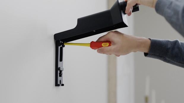 A new Dyson owner screws their Wall dock into place on a wall in their home.