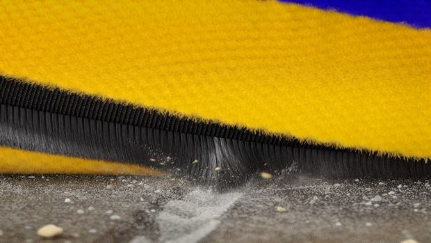 Close-up of the Dyson Fluffy Optic cleaner head’s brush bar as it cleans into a crevice on a hard floor.