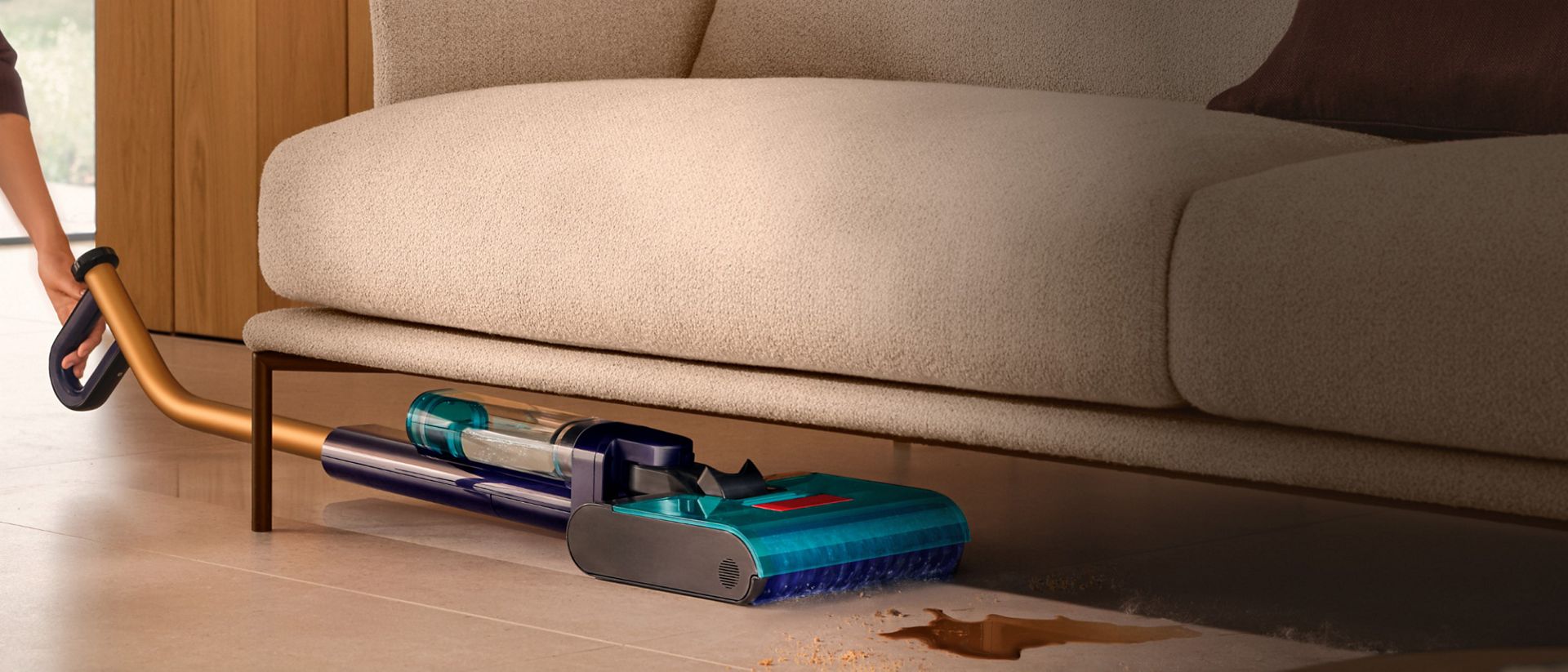 يُستخدم جهاز تنظيف الأرضيات الصلبة Dyson Clean+Wash Hygiene للتنظيف تحت أريكة منخفضة.