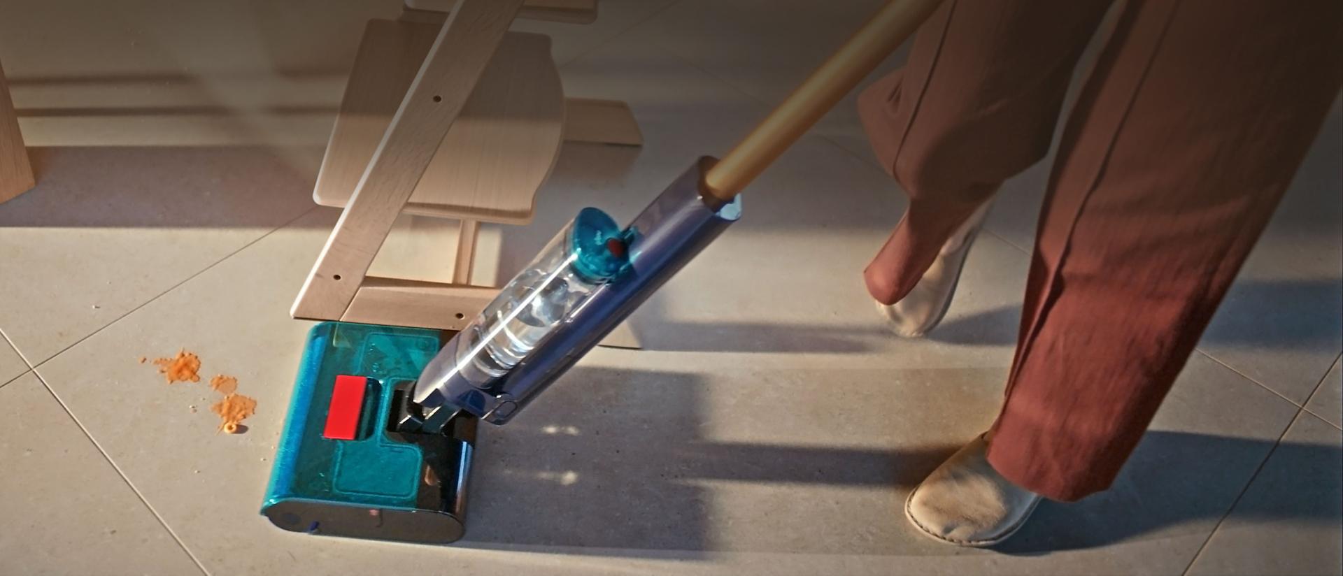 يُنظِّف جهاز تنظيف الأرضيات الصلبة Dyson Clean+Wash Hygiene تحت أريكة.