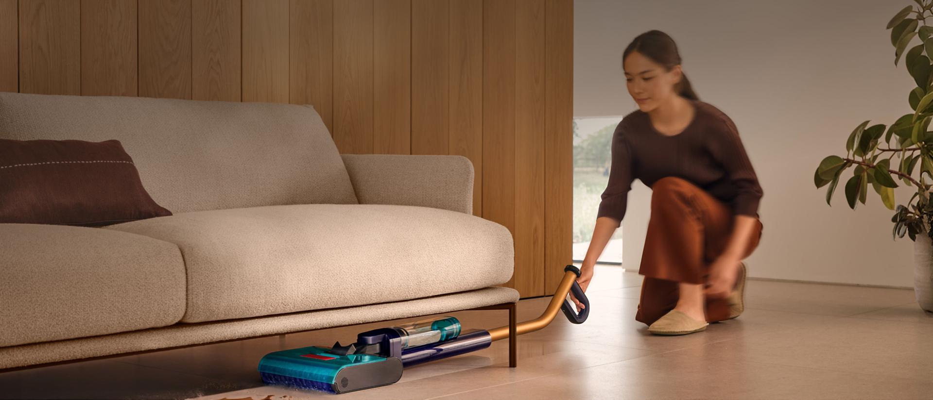 The Dyson Clean+Wash Hygiene hard floor cleaner cleaning under a sofa.