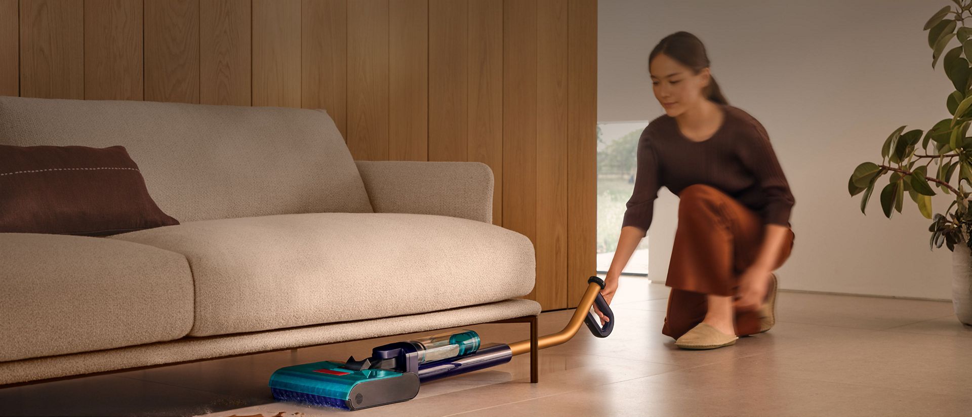 The Dyson Clean+Wash Hygiene hard floor cleaner cleaning under a sofa.