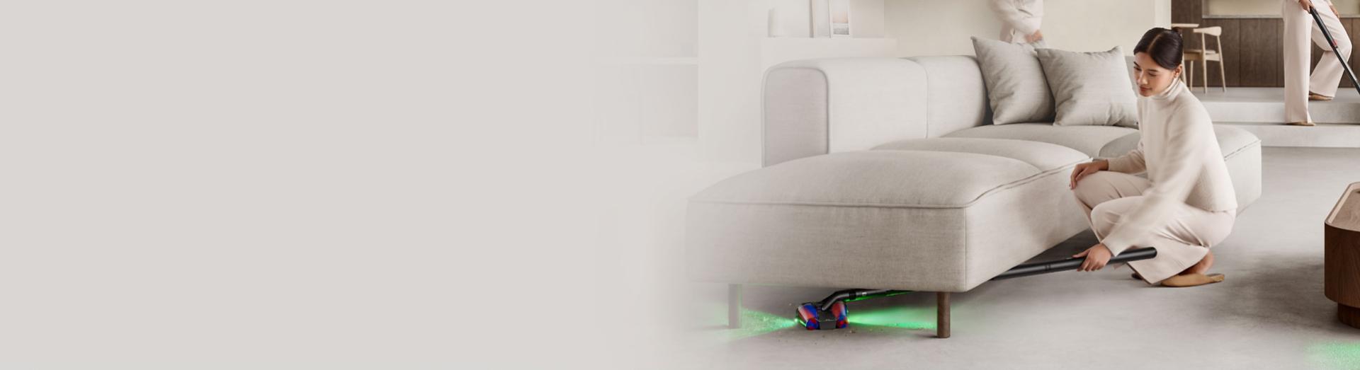 เครื่องดูดฝุ่น Dyson PencilVac Fluffycones ขณะใช้ทำความสะอาดใต้โซฟาทรงเตี้ย