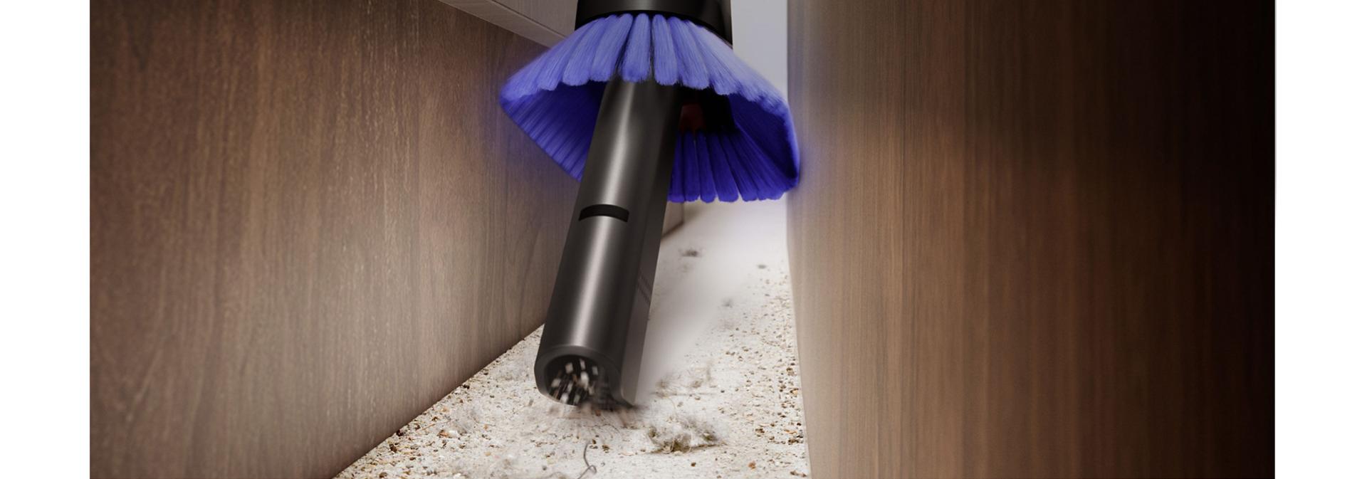 Dyson PencilVac cleaner used to clean a gap between furniture.
