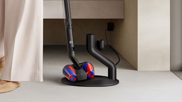 The Dyson PencilVac Fluffycones cleaner is retrieved from its magnetic charging dock.