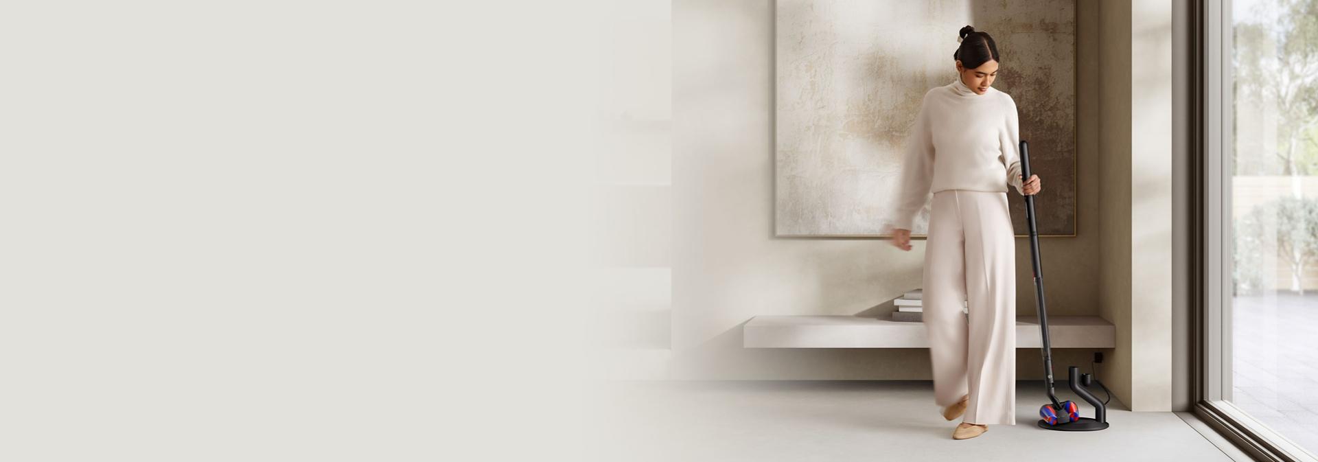 A woman grabs her Dyson PencilVac cleaner from its charging dock.