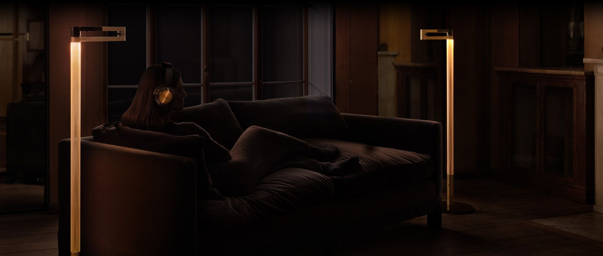 Owner sat listening to her Dyson OnTrac™ headphones on a sofa with the Dyson Solarcycle Morph light behind her.