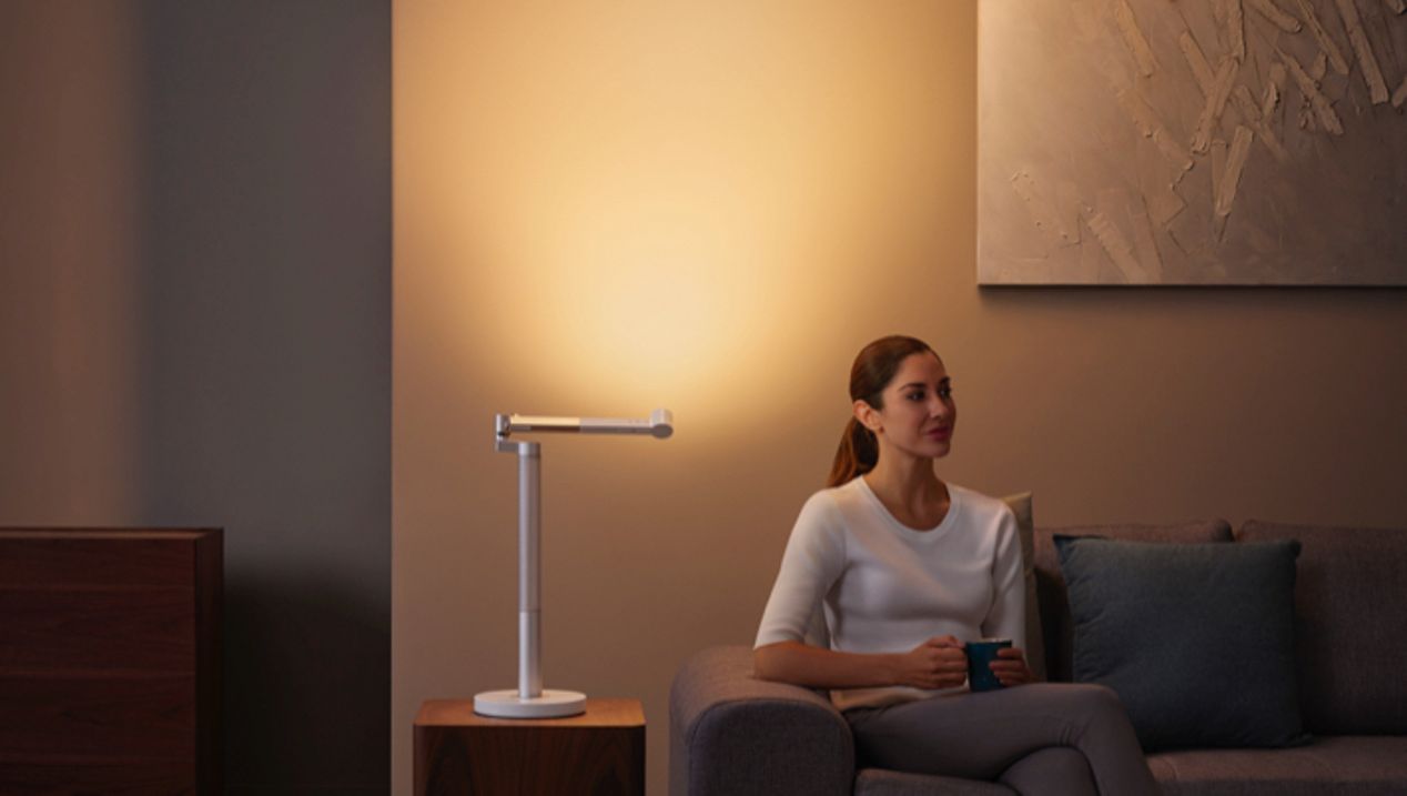 Woman sitting next to the Dyson Lightcycle Morph light in Indirect position
