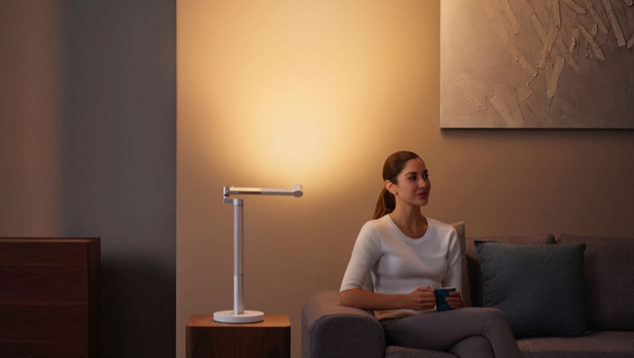 Dyson Lightcycle Morph light in Indirect position Woman sitting next to the Dyson Lightcycle Morph light in Indirect position