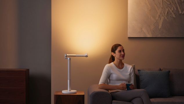 Woman sitting next to the Dyson Lightcycle Morph light in Indirect position