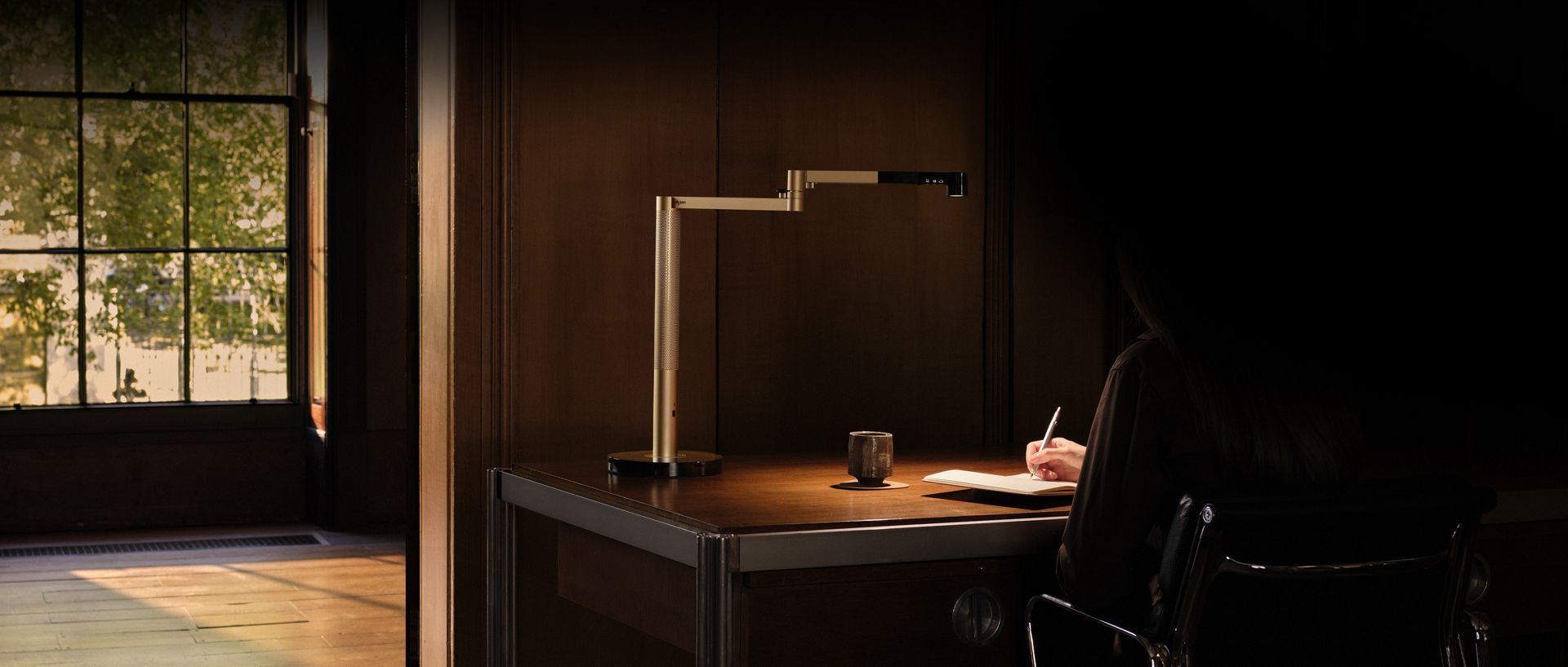 Owner sat at her desk doing work with the Dyson Solarcycle Morph desk light.