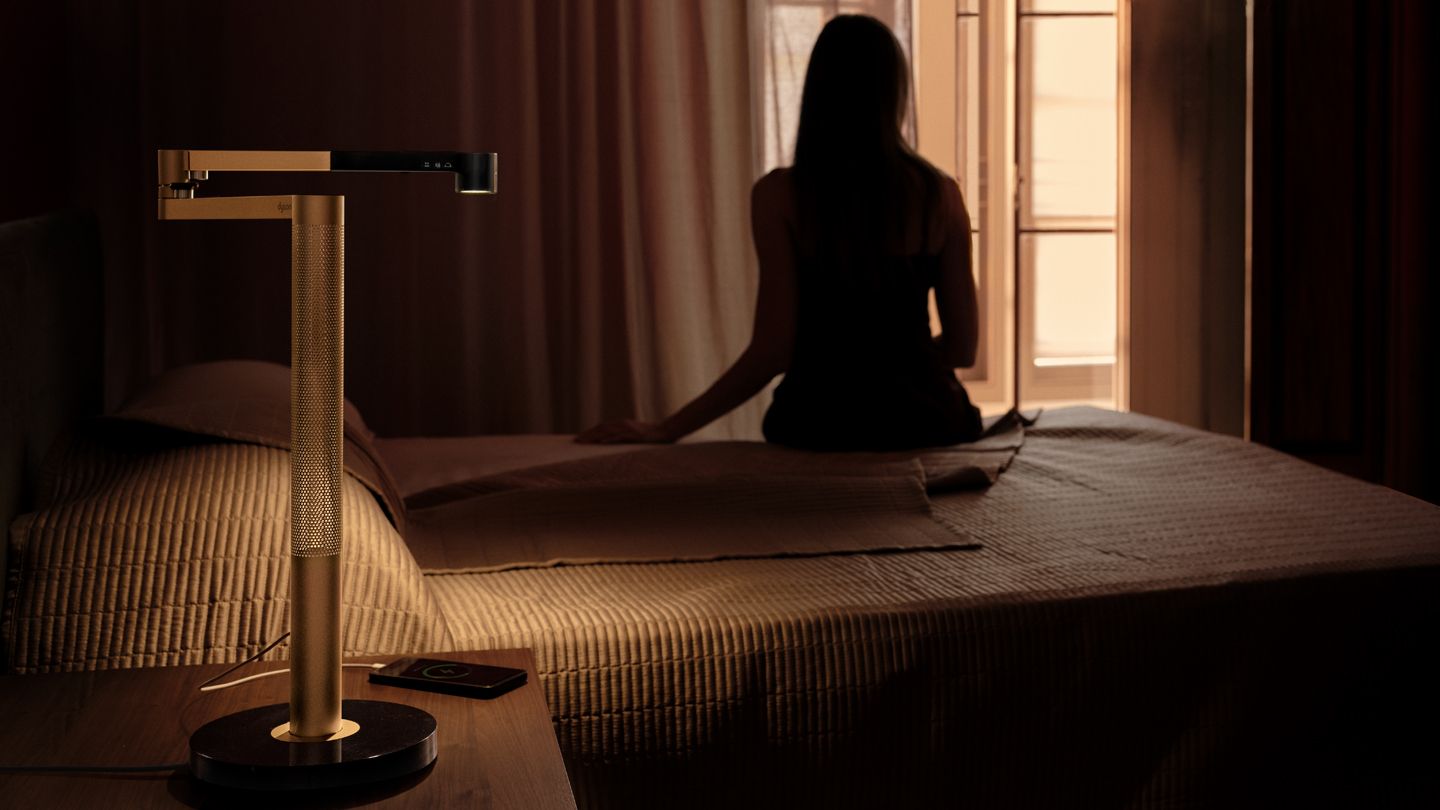 Owner sat on the edge of her bed with the Dyson Solarcycle Morph desk light on her bedside table.