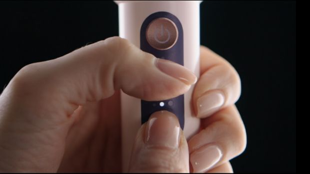 Laikomi nuspausti „Dyson CameraJet“ dantų šepetėlio valdymo mygtukai.