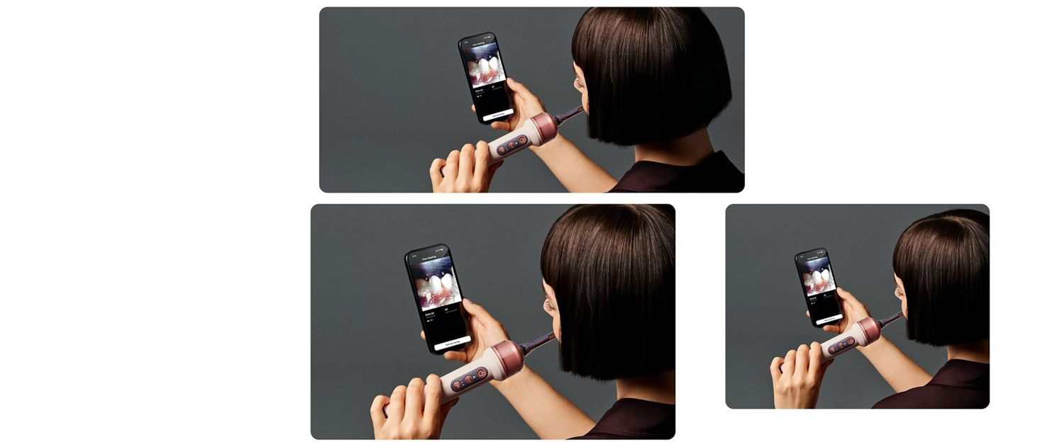 Person holding a smartphone displaying a toothbrush-related app while an electric toothbrush is positioned nearby.