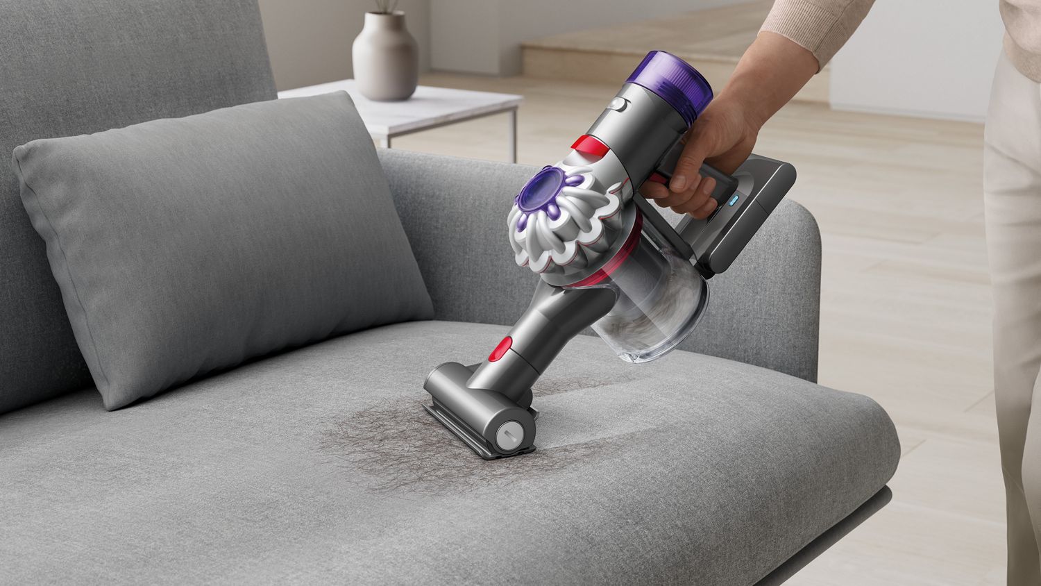 The Dyson Car+Boat handheld vacuum with the Mini motorised tool cleaning hair from a sofa.