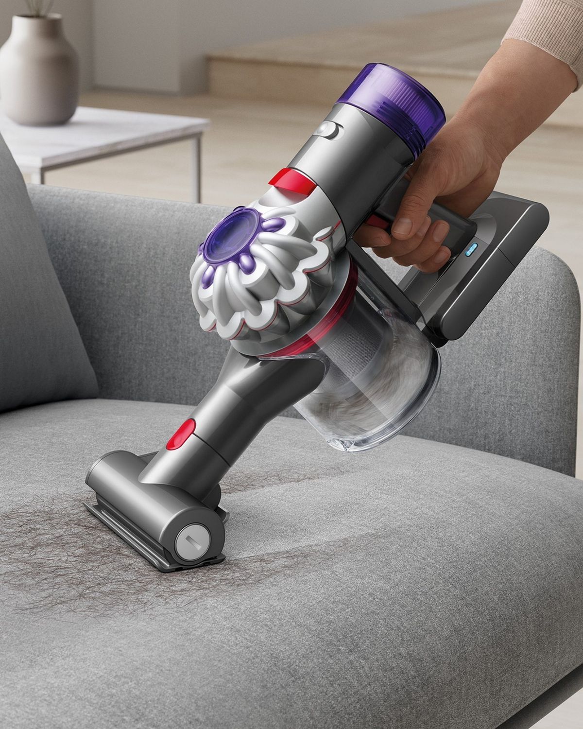 The Dyson Car+Boat handheld vacuum with the Mini motorised tool cleaning hair from a sofa.