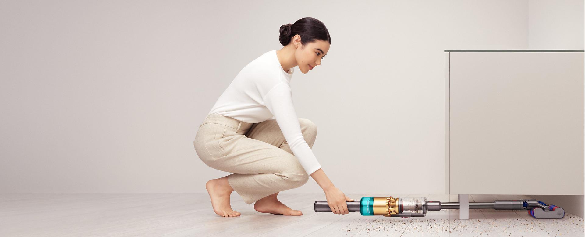 다이슨 옴니-글라이드™ 무선 청소기로 장식장 아래를 청소하는 여성.