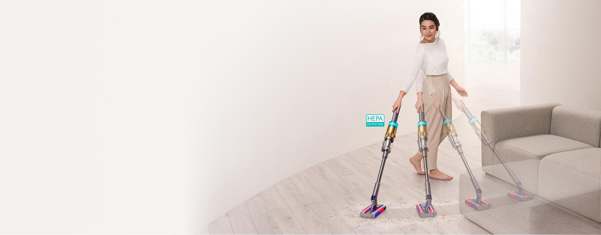다이슨 옴니-글라이드 무선 청소기로 소파 주변의 마룻바닥을 청소하는 여성.