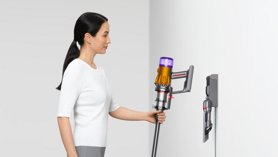 Frau legt Dyson Akkustaubsauger auf die Wand montierte Ladestation ab