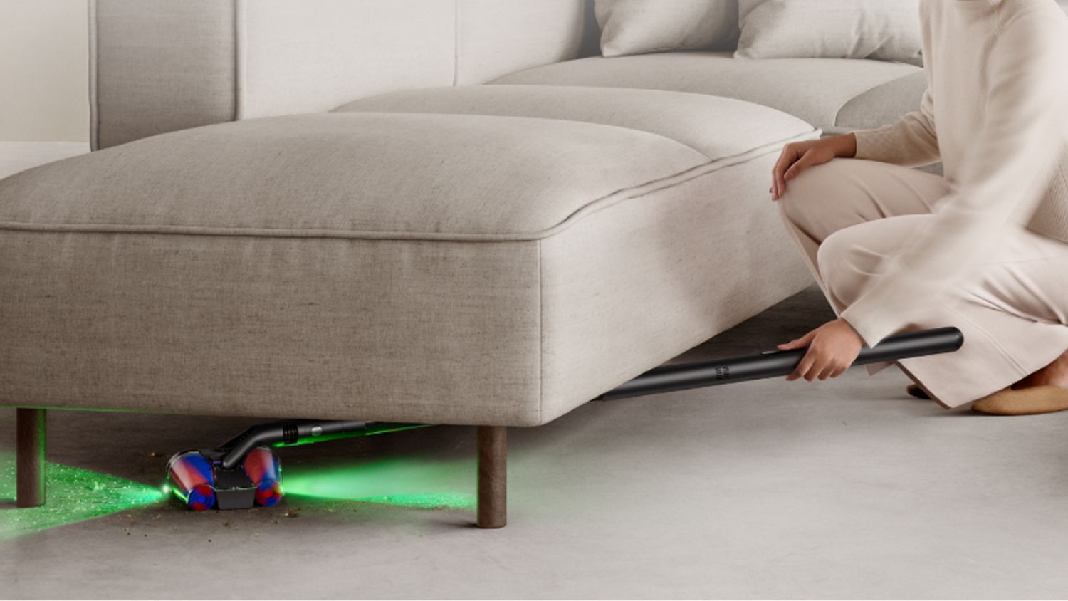 A Dyson PencilVac cleaning underneath a sofa showcasing the illumination technology in dark spaces.